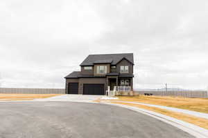 View of front of home with a garage, concrete driveway, a shingled roof, and fence