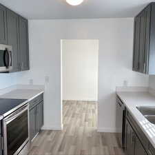 Kitchen with appliances with stainless steel finishes, light countertops, light wood-style floors, and gray cabinetry