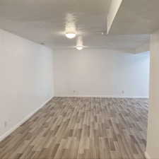 Finished below grade area featuring light wood-style floors, baseboards, and a textured ceiling