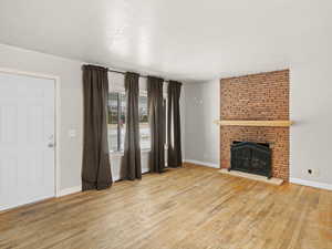 Unfurnished living room with light wood-type flooring, a fireplace, a textured ceiling, and baseboards