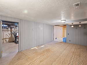 Finished below grade area with light colored carpet, visible vents, and a textured ceiling