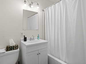 Bathroom featuring toilet, shower / bathtub combination with curtain, and vanity