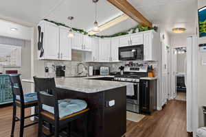 Kitchen featuring black microwave, a sink, light countertops, hanging light fixtures, and stainless steel gas stove