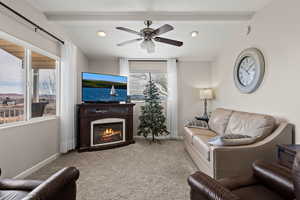 Living area featuring a glass covered fireplace, light carpet, lofted ceiling with beams, and baseboards