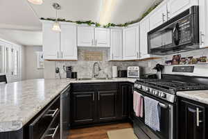 Kitchen featuring a sink, white cabinets, hanging light fixtures, dark cabinetry, and black appliances