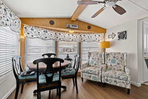 Dining area featuring lofted ceiling with beams, ceiling fan, wood walls, wood finished floors, and baseboards