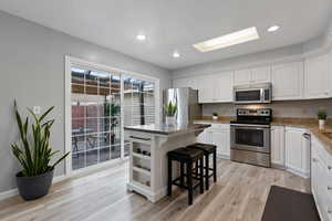 Kitchen with a breakfast bar, a center island, stainless steel appliances, light wood-style floors, and white cabinetry