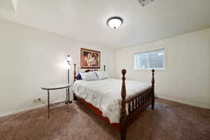 Bedroom with a textured ceiling, dark carpet, visible vents, and baseboards