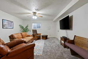 Living area featuring baseboards, visible vents, light colored carpet, ceiling fan, and a textured ceiling