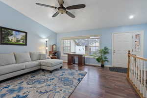 Living area with dark wood-style flooring, vaulted ceiling, baseboards, and ceiling fan