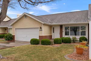 Ranch-style house with an attached garage, a shingled roof, a front lawn, and brick siding