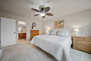 Bedroom featuring a ceiling fan, light colored carpet, and ensuite bath