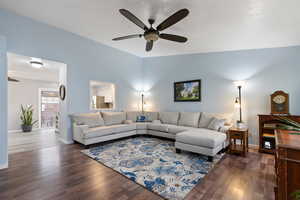 Living room featuring dark wood-type flooring, a ceiling fan, and baseboards