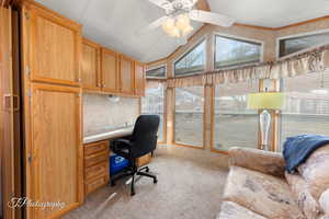 Office area featuring ceiling fan, light carpet, vaulted ceiling, and built in study area