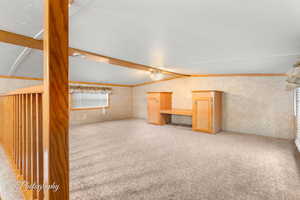 Unfurnished living room featuring lofted ceiling with beams, ornamental molding, and light colored carpet