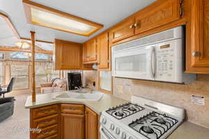 Kitchen with white appliances, brown cabinets, a peninsula, light countertops, and a sink