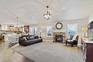 Living area with vaulted ceiling, a notable chandelier, a stone fireplace, and baseboards