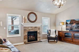 Living room featuring light carpet, lofted ceiling, baseboards, and a stone fireplace