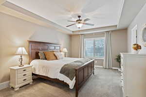 Bedroom featuring baseboards, a tray ceiling, visible vents, and light colored carpet