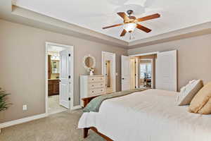 Bedroom featuring light carpet, a tray ceiling, connected bathroom, and baseboards