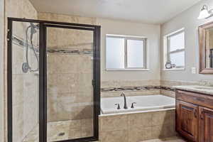 Bathroom featuring a textured ceiling, a stall shower, a garden tub, and vanity