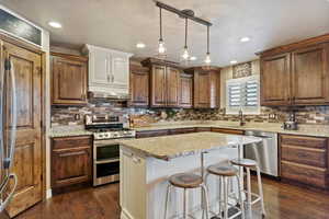 Kitchen featuring under cabinet range hood, stainless steel appliances, a sink, a kitchen island, and dark wood finished floors