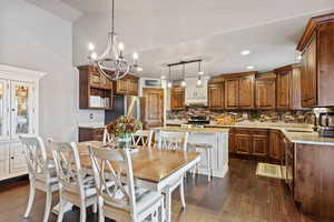 Dining area with dark wood-style floors, high vaulted ceiling, a notable chandelier, and recessed lighting