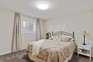 Bedroom with dark colored carpet, visible vents, a textured ceiling, and baseboards