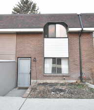 Entrance to property with roof with shingles, brick siding, and mansard roof