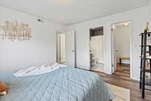 Bedroom with ensuite bathroom, wood finished floors, visible vents, and baseboards