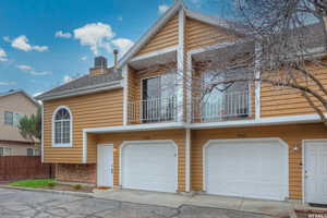 View of front of house featuring roof with shingles, a chimney, fence, a balcony, and stone siding