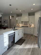 Kitchen featuring decorative light fixtures, freestanding refrigerator, a sink, premium range hood, and dishwashing machine