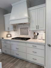 Kitchen with tasteful backsplash, stainless steel gas cooktop, wood finished floors, premium range hood, and white cabinetry