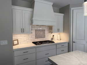 Kitchen with stainless steel gas cooktop, white cabinets, backsplash, custom exhaust hood, and light stone countertops