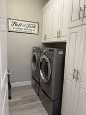 Clothes washing area with cabinet space, baseboards, washer and clothes dryer, and light wood finished floors