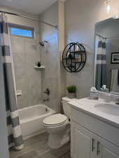 Full bathroom featuring toilet, vanity, wood finished floors, and shower / tub combo with curtain