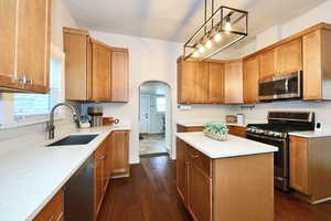 Kitchen with arched walkways, a sink, light countertops, appliances with stainless steel finishes, and pendant lighting