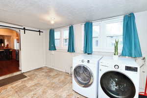 Washroom with washing machine and dryer, laundry area, a healthy amount of sunlight, and a barn door