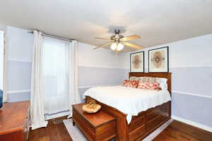 Bedroom featuring a textured ceiling, dark wood-style flooring, visible vents, baseboards, and a ceiling fan