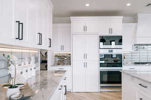 Kitchen featuring light stone countertops, white cabinetry, and wall chimney range hood