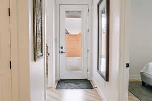 Doorway to outside with light wood-style flooring and baseboards