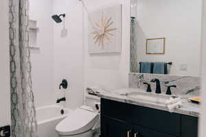 Bathroom featuring toilet, shower / bathtub combination with curtain, and vanity