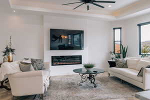 Living room with recessed lighting, a tray ceiling, wood finished floors, and a glass covered fireplace