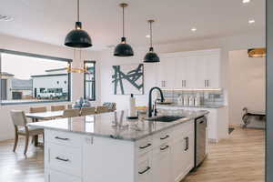 Kitchen with light stone counters, decorative light fixtures, white cabinetry, a sink, and an island with sink