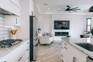 Kitchen featuring a tray ceiling, open floor plan, premium range hood, and light stone countertops