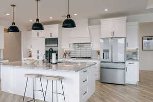 Kitchen with appliances with stainless steel finishes, premium range hood, a center island with sink, and white cabinetry