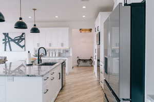 Kitchen featuring pendant lighting, an island with sink, a sink, and white cabinets