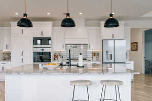 Kitchen featuring light stone countertops, a kitchen island with sink, refrigerator with ice dispenser, and white cabinets