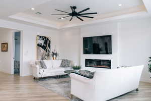 Living area with light wood-type flooring, a tray ceiling, and a glass covered fireplace