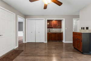 Interior space with dark wood-style flooring, a sink, a ceiling fan, and baseboards